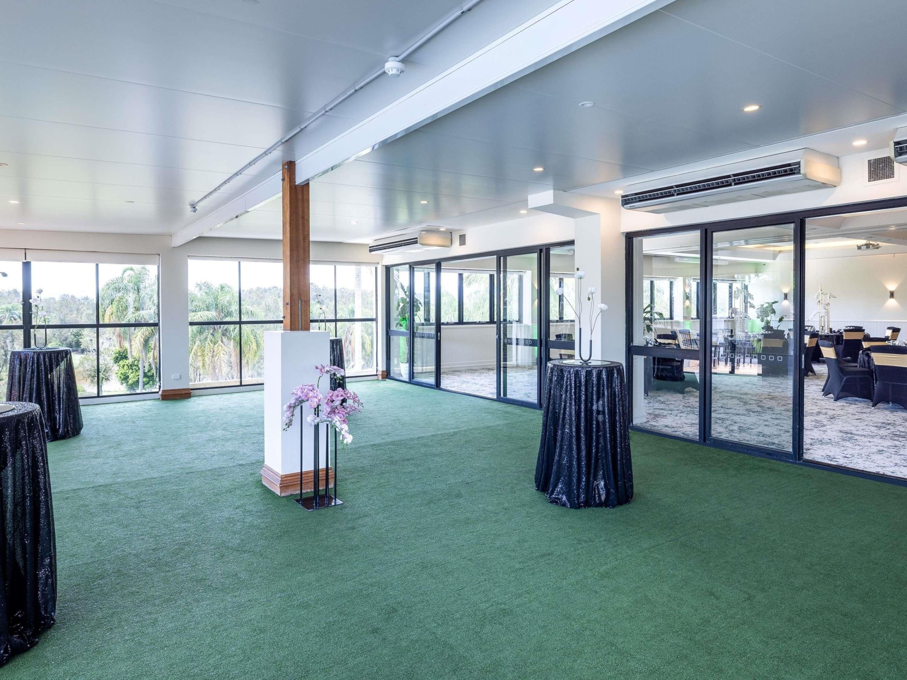 A spacious indoor area with a green carpet, large windows, and a seating area with tables and chairs.