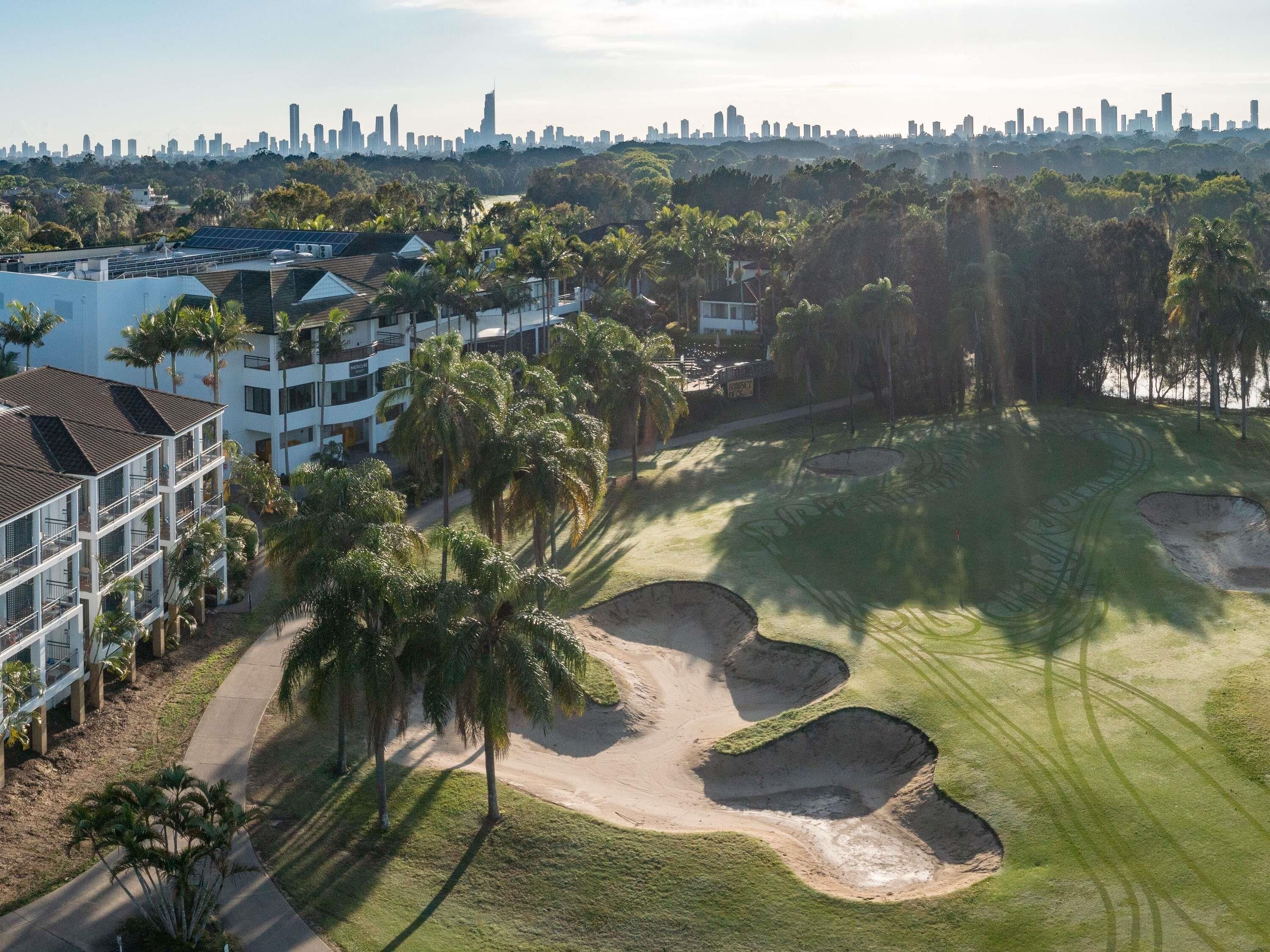 A golf course with bunkers and palm trees, surrounded by a city skyline.