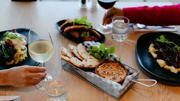 Una mesa de comedor con diversos platos, vasos de agua y vino, y una cesta de pan plano.
