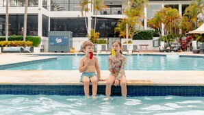 Two children sitting by a pool with a building in the background. - Mercure Gold Coast Resort (Carrara)