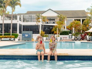 Two children sitting by a pool with a building in the background. - Mercure Gold Coast Resort (Carrara)