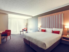 Habitación de hotel con una cama grande, un escritorio, una silla y una mesita de noche con lámpara.