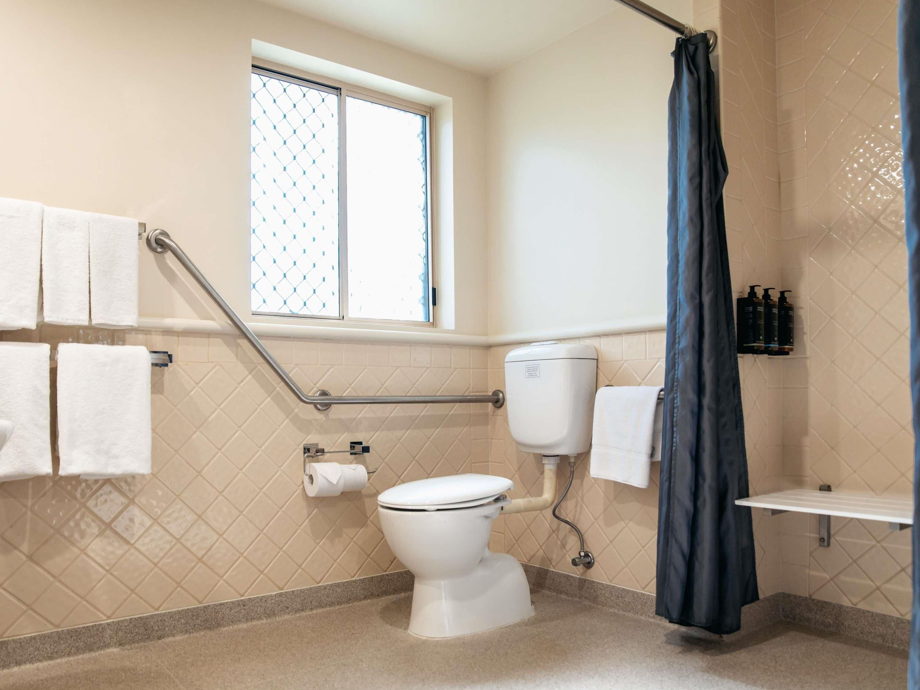 A bathroom with a toilet, a window, a shower curtain, and a towel rack.