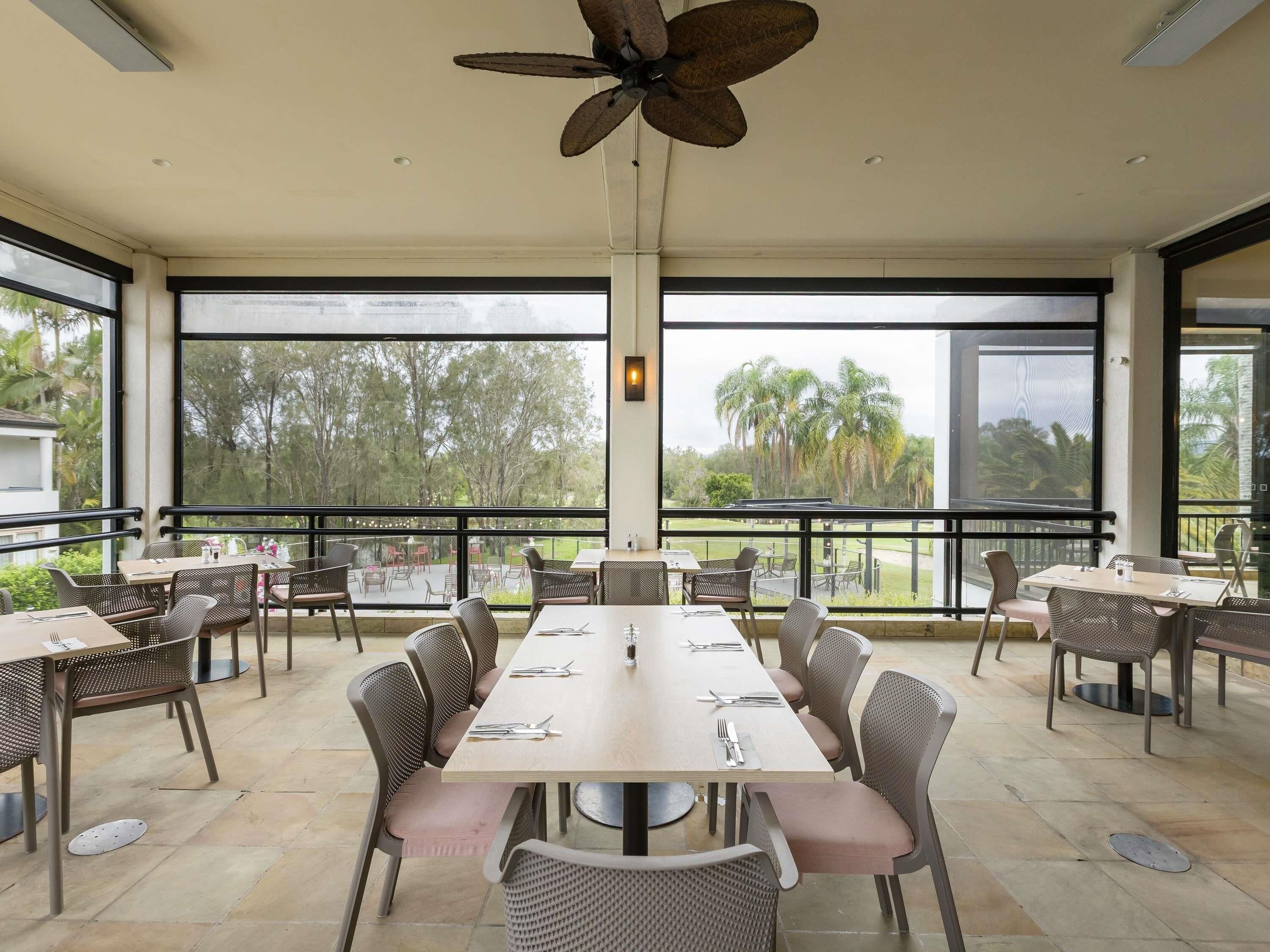 Un restaurante con terraza, amplios ventanales y ventilador de techo.