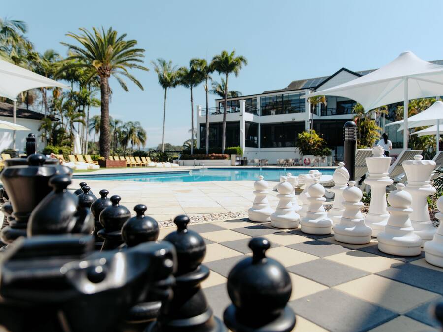A poolside chess set with a pool and palm trees in the background.