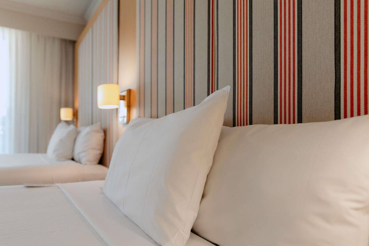 A hotel room with a bed, pillows, striped wallpaper, and a lamp.