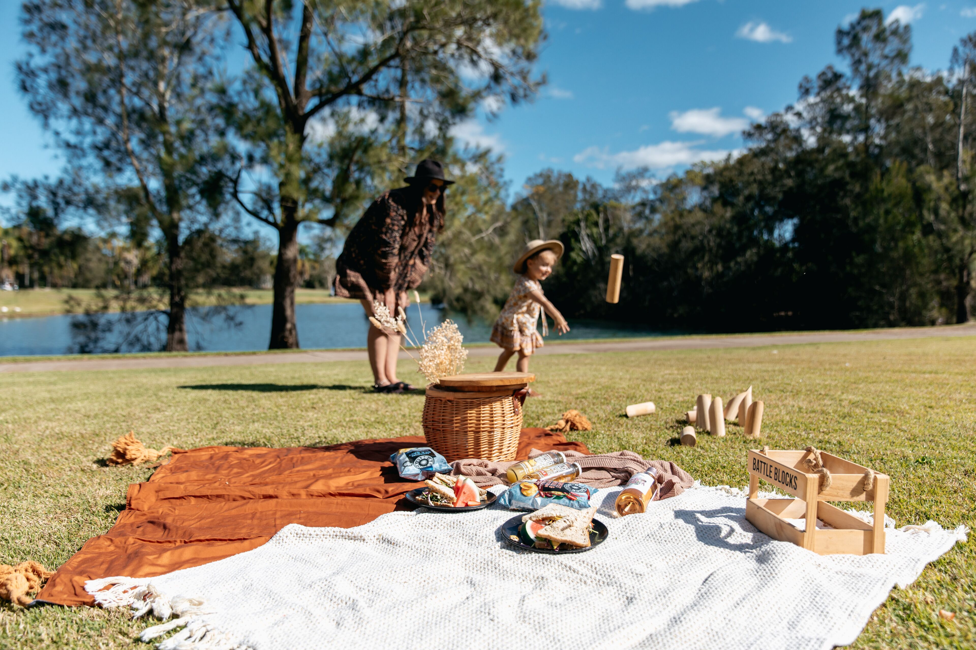 A picnic setup on a grassy area with a blanket, food items, and a basket.