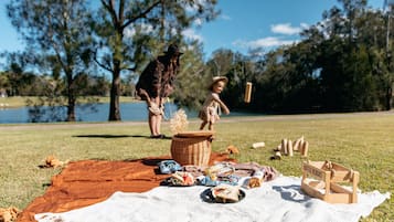 A picnic setup on a grassy area with a blanket, food items, and a basket.