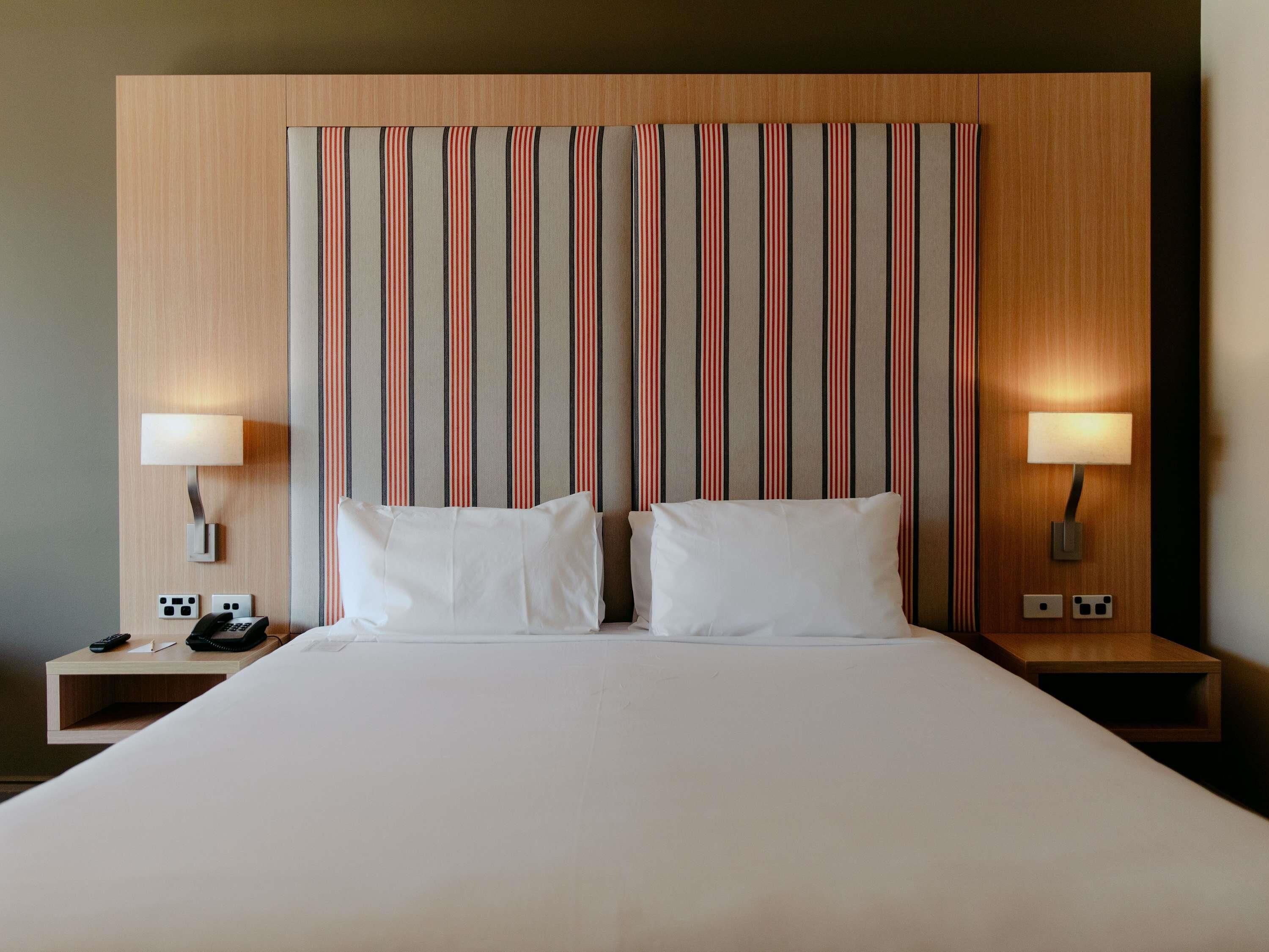 Hotelkamer met een groot bed, twee bedlampjes, een nachtkastje met telefoon en een gestreept hoofdeinde.