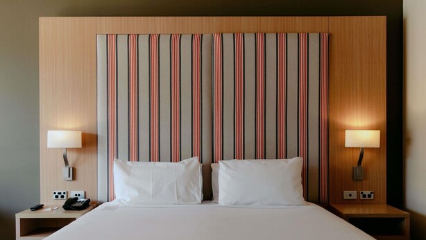 Habitación de hotel con una cama grande, dos lámparas de noche, una mesita de noche con teléfono y un cabecero a rayas.