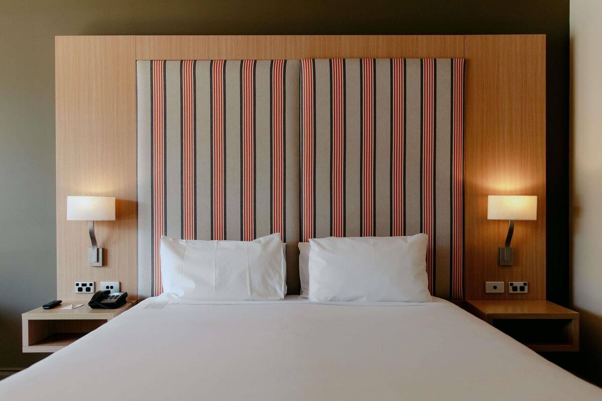 A hotel room with a large bed, two bedside lamps, a nightstand with a phone, and a striped headboard.