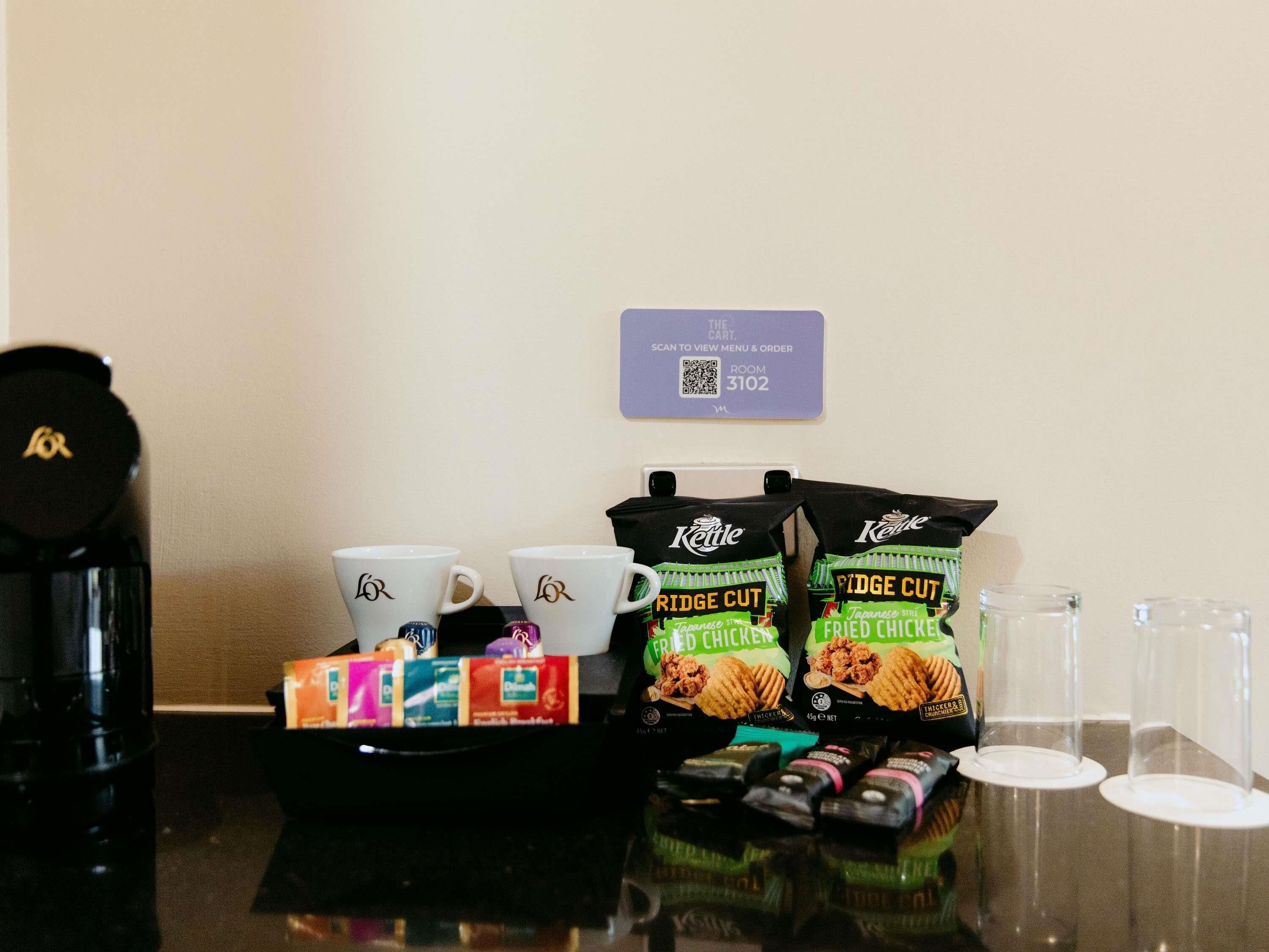 A coffee station with two white cups, a kettle, a tray with snacks, and a QR code for room 3102.
