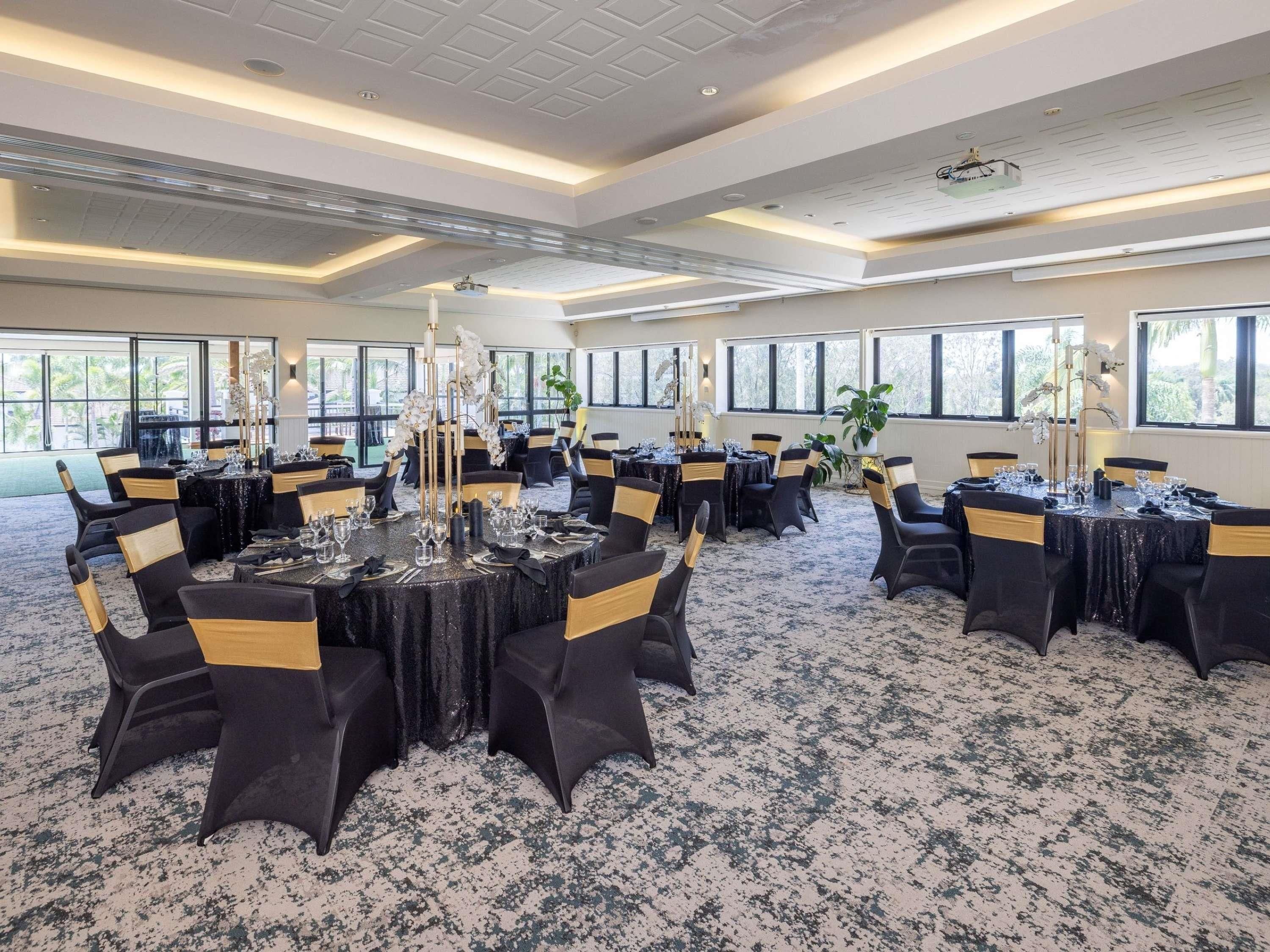 Une salle de conférence avec des tables rondes, des chaises noires ornées de rubans dorés et un sol recouvert de moquette.