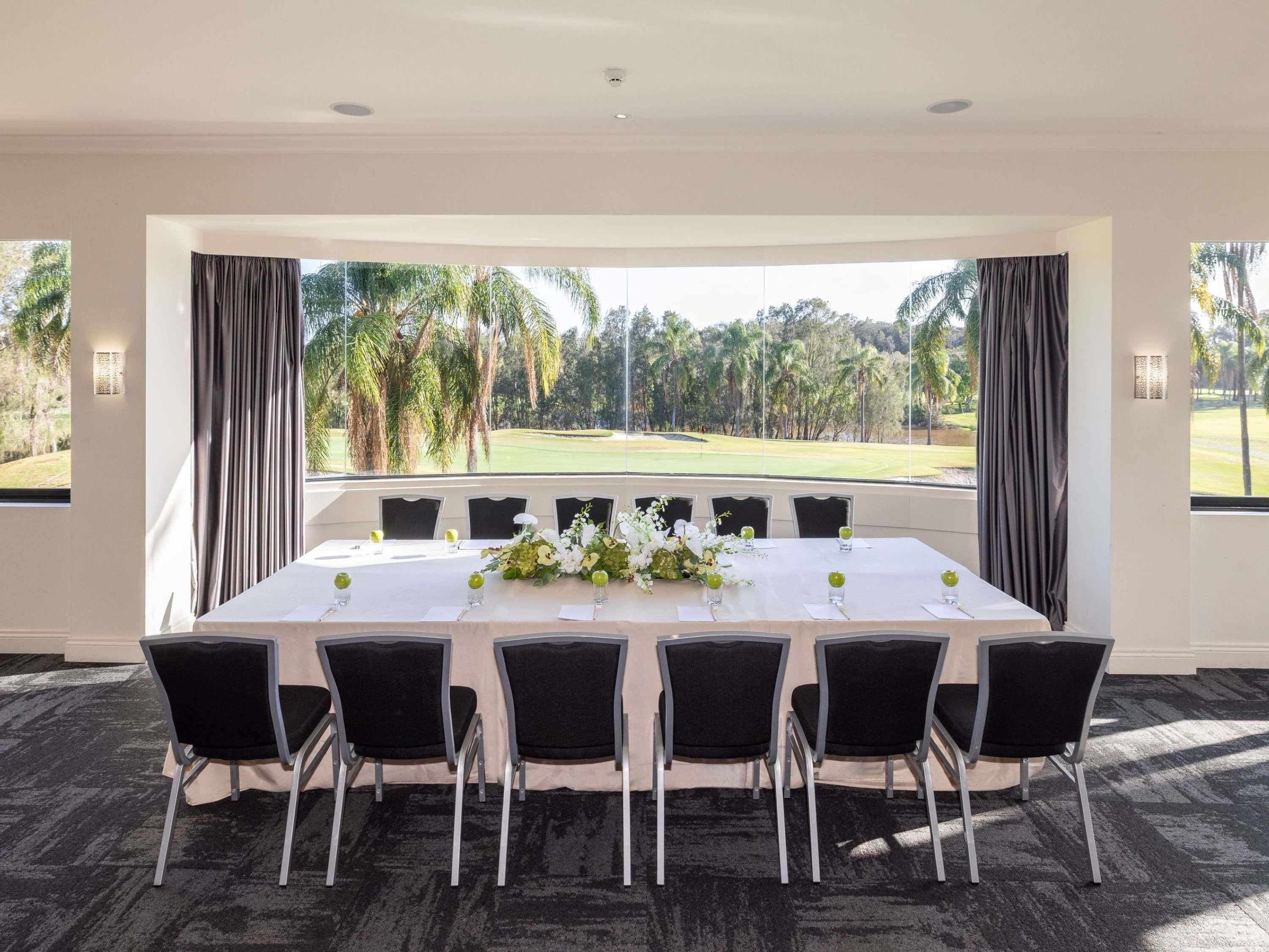 Une salle de conférence avec vue sur un terrain de golf, une longue table entourée de chaises et un arrangement floral en guise de décoration centrale.
