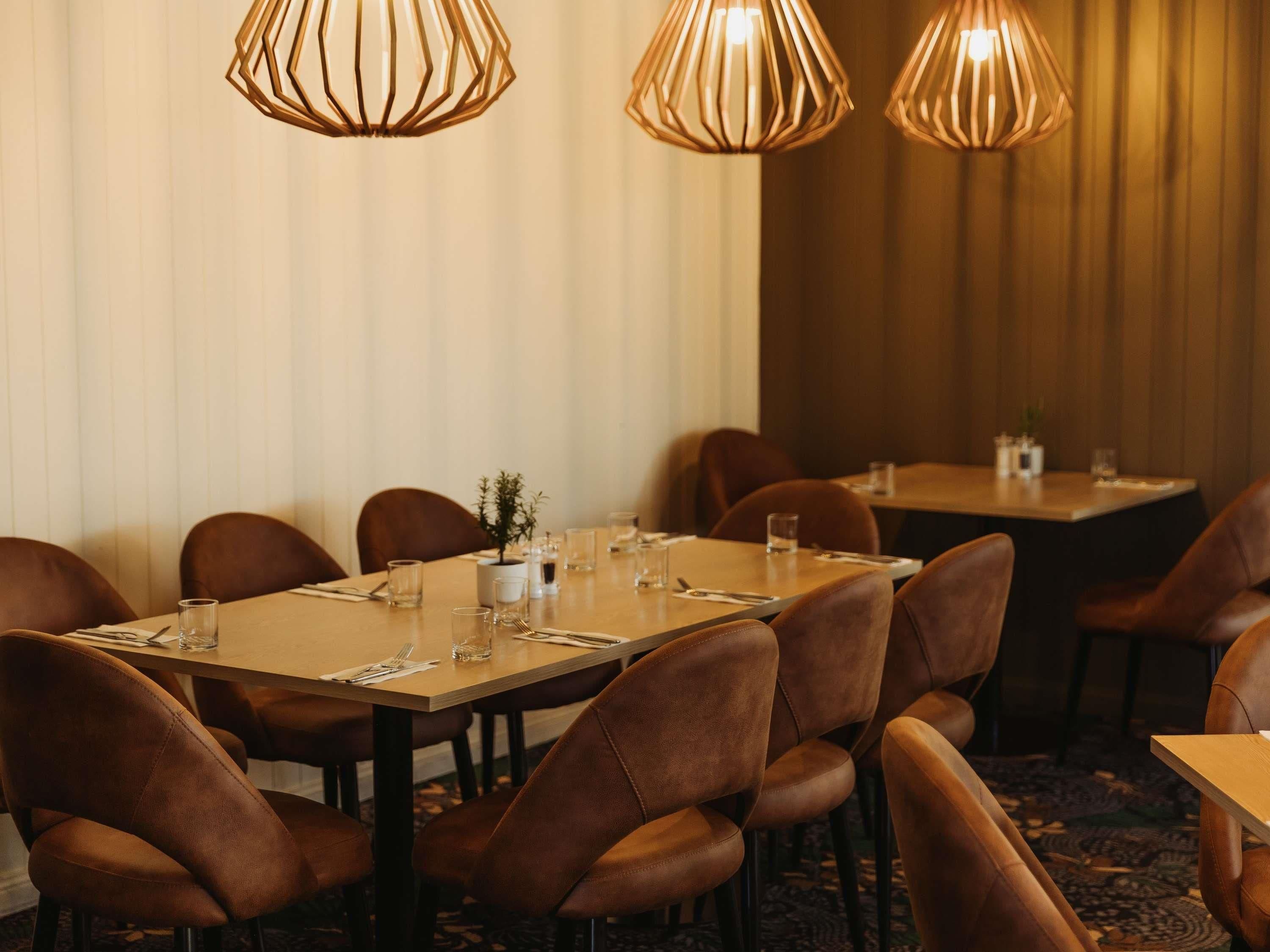 A dining area with tables set for four, brown leather chairs, and pendant lighting.