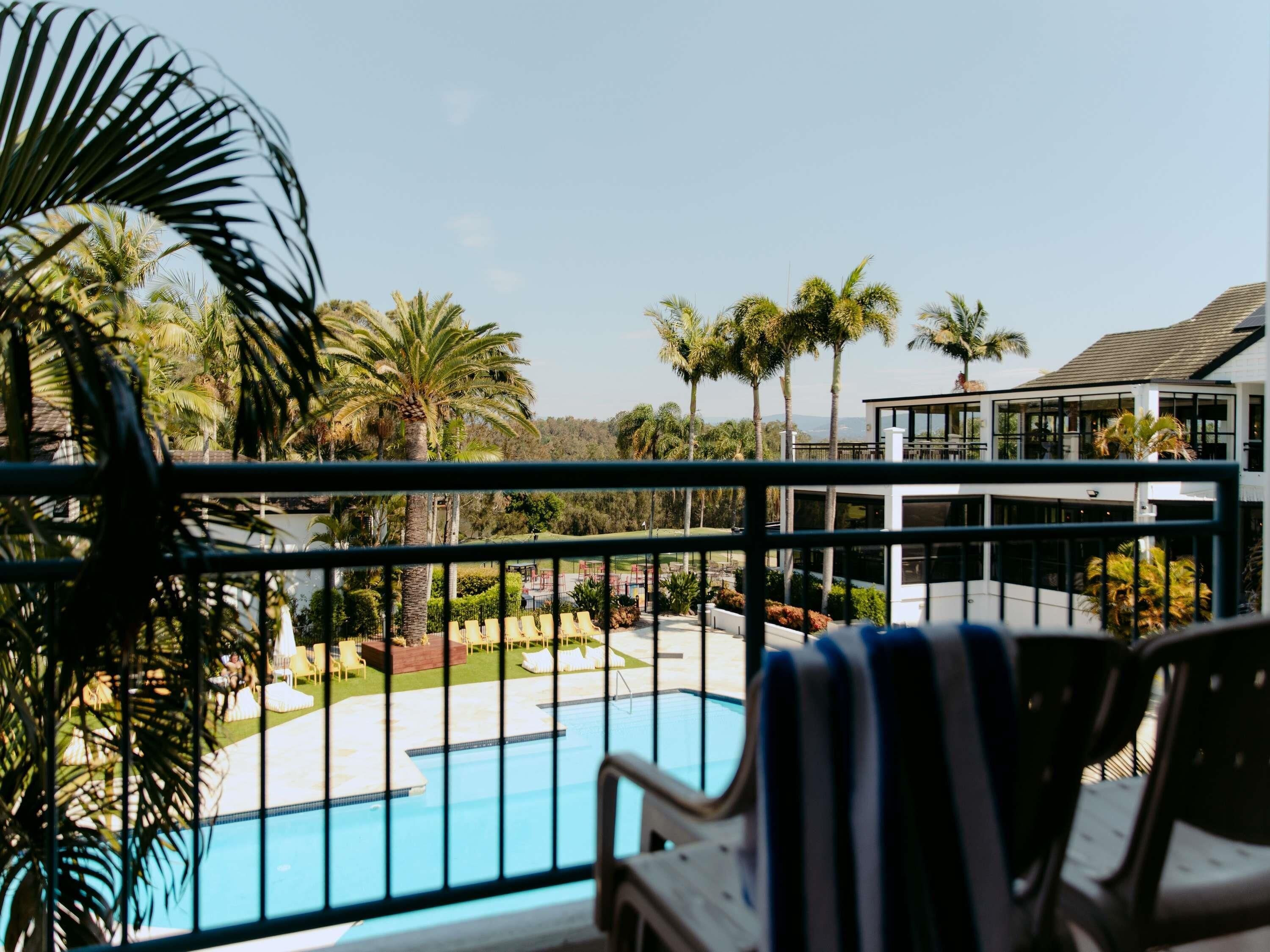 A poolside view with a clear blue pool, lounge chairs, and palm trees.