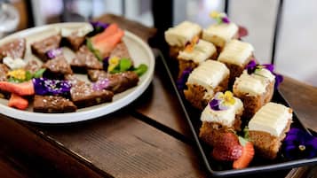 A wooden table with two plates of food, one with brownies and strawberries, the other with cupcakes and flowers.