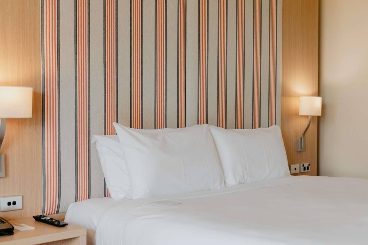 A hotel room with a bed, two bedside lamps, a nightstand, and a striped wall.