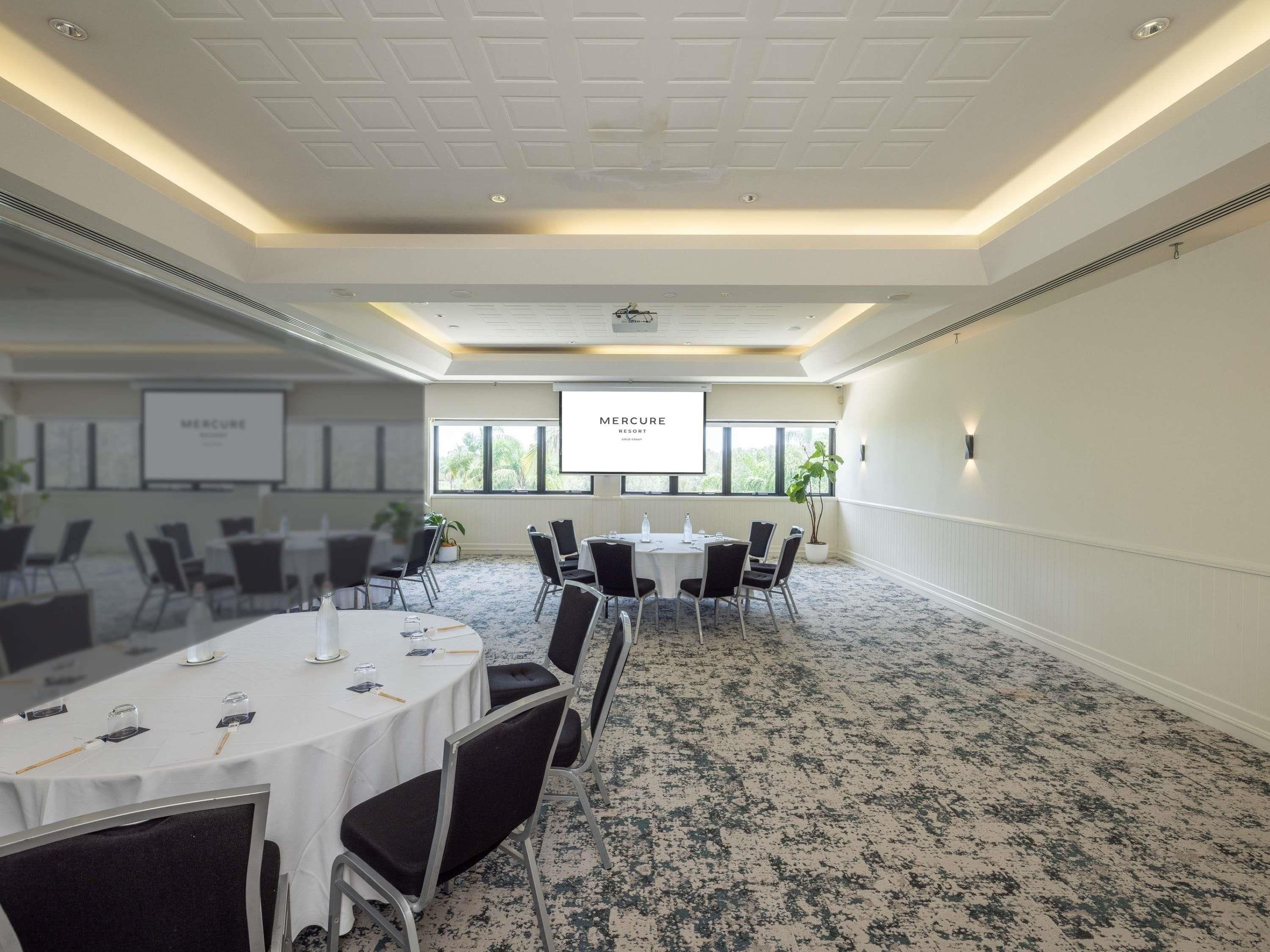 Una sala conferenze con uno schermo per proiettore, tavoli, sedie e pavimento rivestito di moquette.