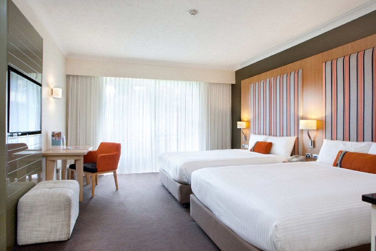 A hotel room with two beds, a desk, and a chair.