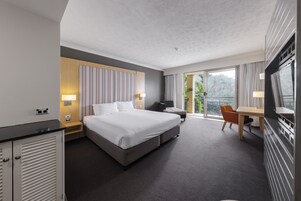 Una habitación de hotel moderna con una cama grande, un escritorio y una silla. Tiene un balcón con vista a zonas verdes.