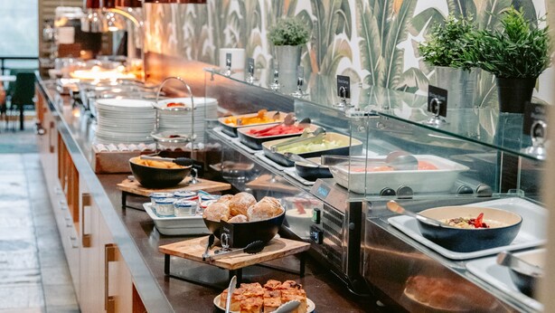 A buffet with various food options, a patterned wall, and a potted plant. - Mercure Gold Coast Resort (Carrara)