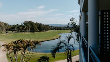 Vista de un campo de golf con un cuerpo de agua, palmeras y un edificio al frente.