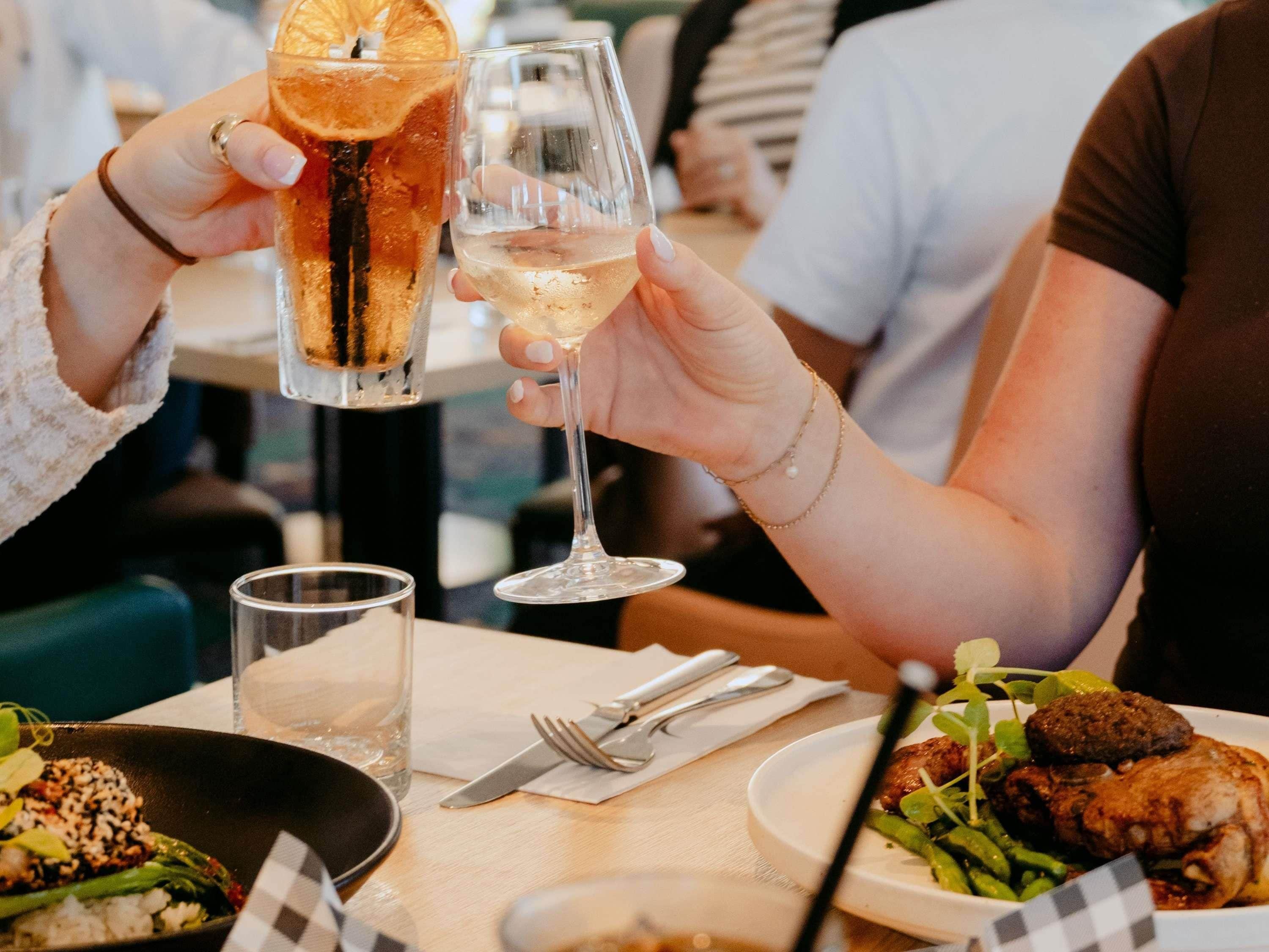 Een eettafel met een bord eten, een glas witte wijn en een glas ijskoud drankje met een schijfje sinaasappel.