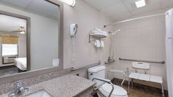 A bathroom with a granite countertop sink, a toilet, a shower with a grab bar, a hairdryer, and a towel rack.