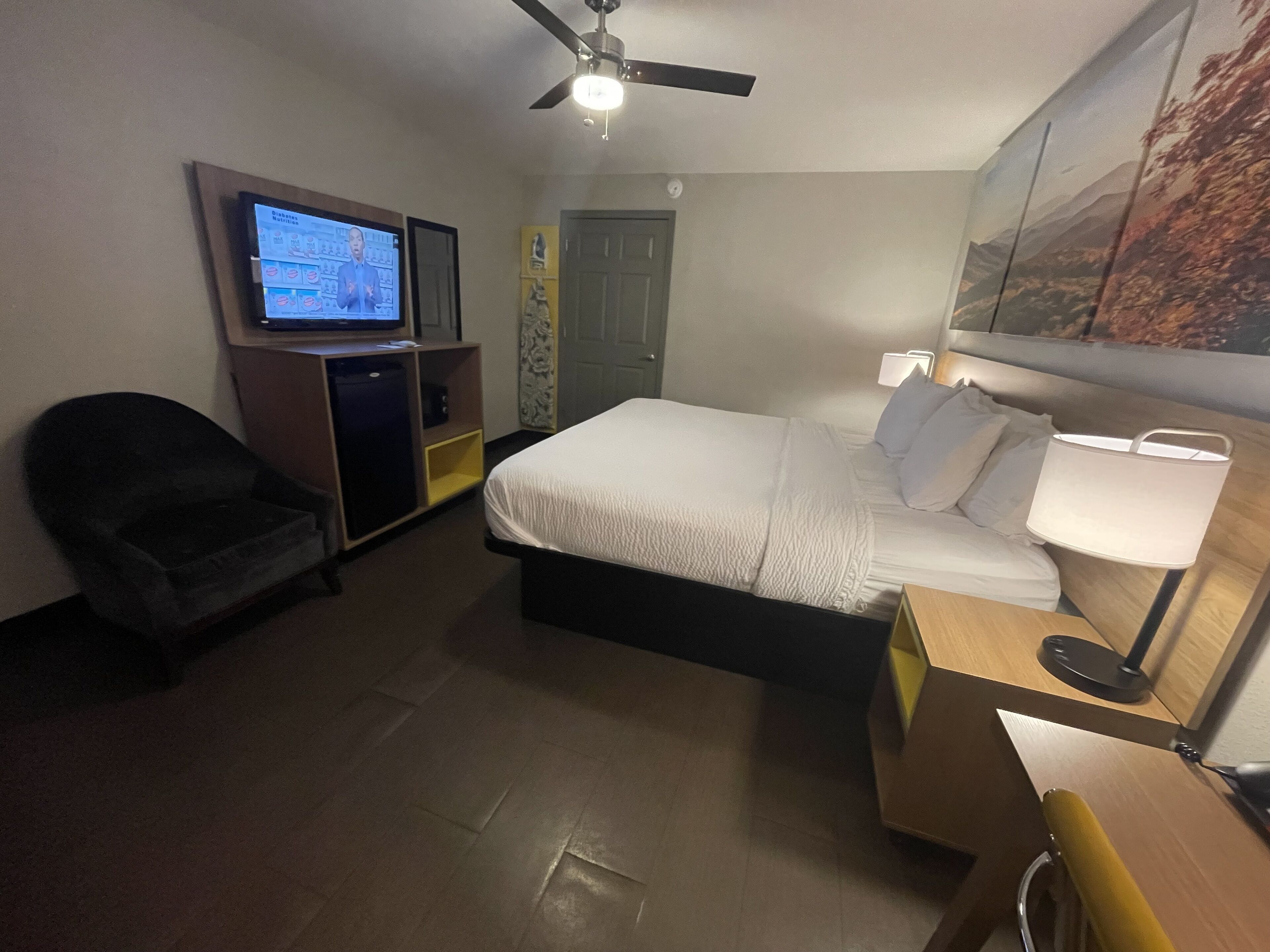 A hotel room with a bed, a desk, a chair, a television, and a ceiling fan.