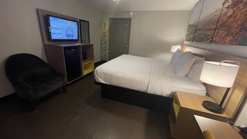 A hotel room with a bed, a desk, a chair, a television, and a ceiling fan.