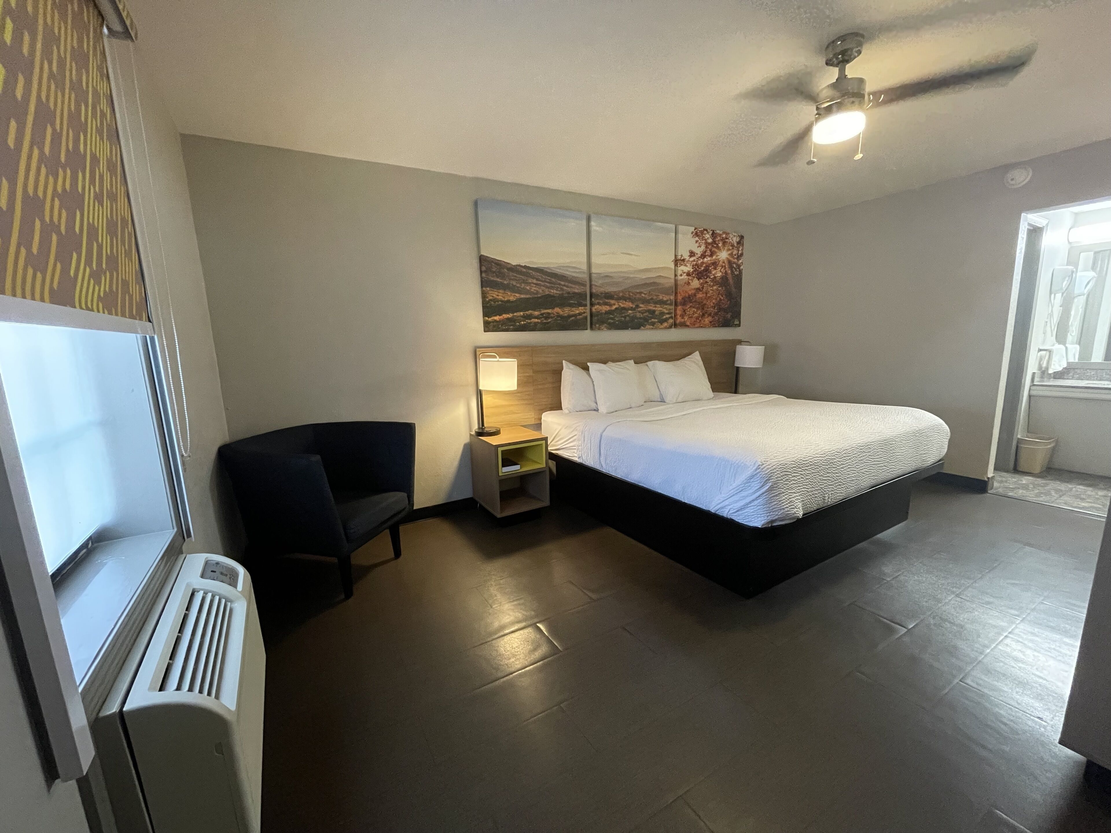 Ein modernes Hotelzimmer mit einem großen Bett, einem Schreibtisch, einem Sessel, einem Fernseher und einem Deckenventilator.