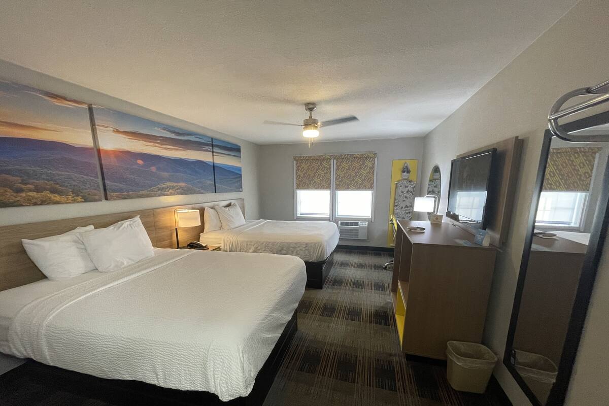 A hotel room with two beds, a desk, a TV, and a ceiling fan.
