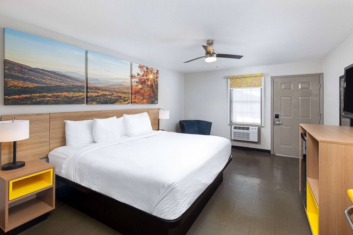 A hotel room with a large bed, a desk, a chair, a ceiling fan, and artwork on the wall.