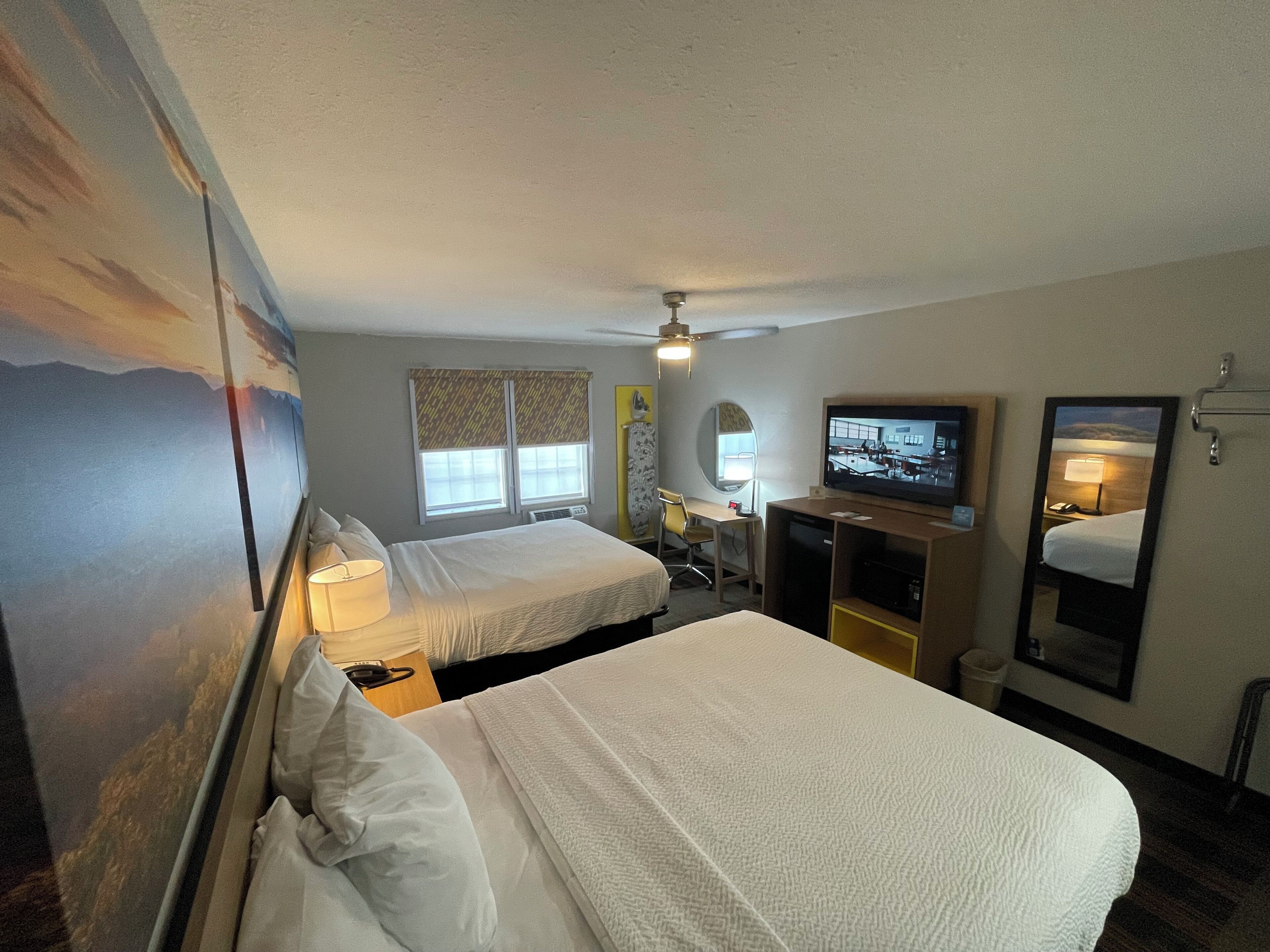 A hotel room with two beds, a desk with a chair, a television, and a large mirror.