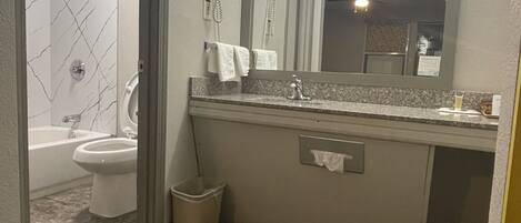A bathroom with a marble wall, a sink, a mirror, a hairdryer, and a shower.