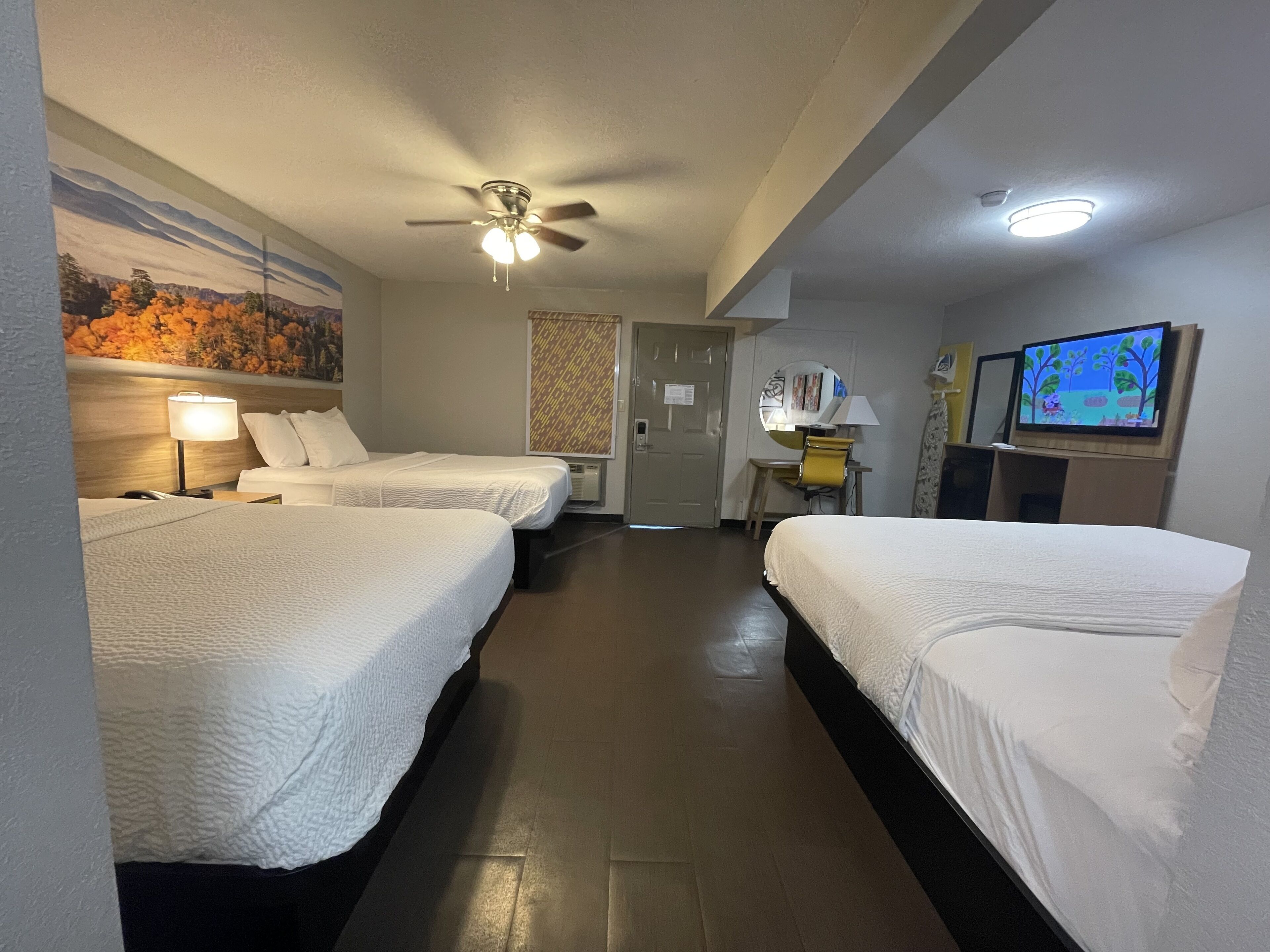 Habitación de hotel con dos camas, un ventilador de techo, un televisor y un escritorio con una silla.
