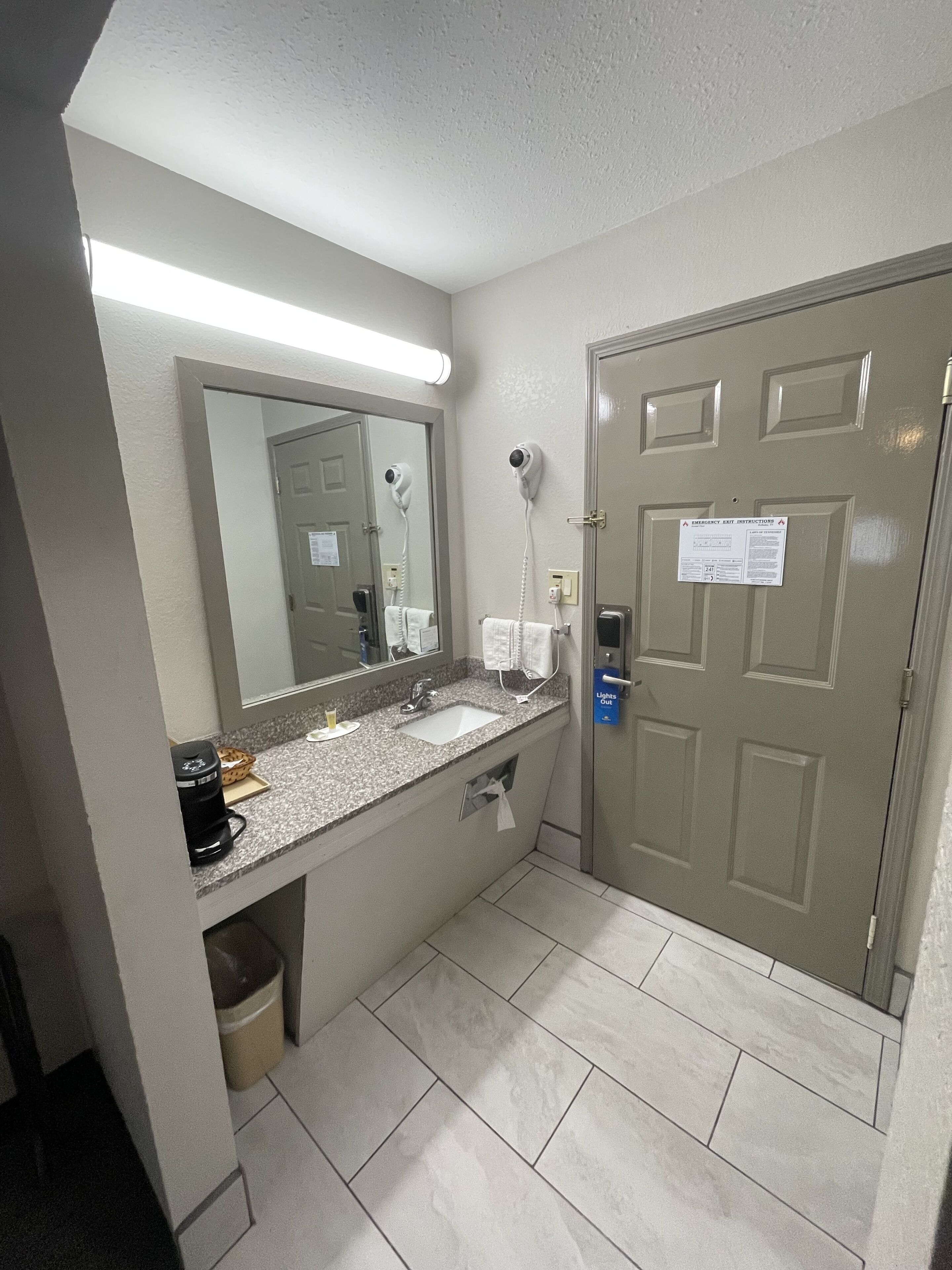 A hotel bathroom with a sink, mirror, hairdryer, and towel dispenser.