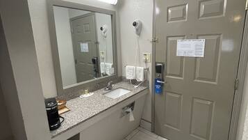 A hotel bathroom with a sink, mirror, hairdryer, and towel dispenser.