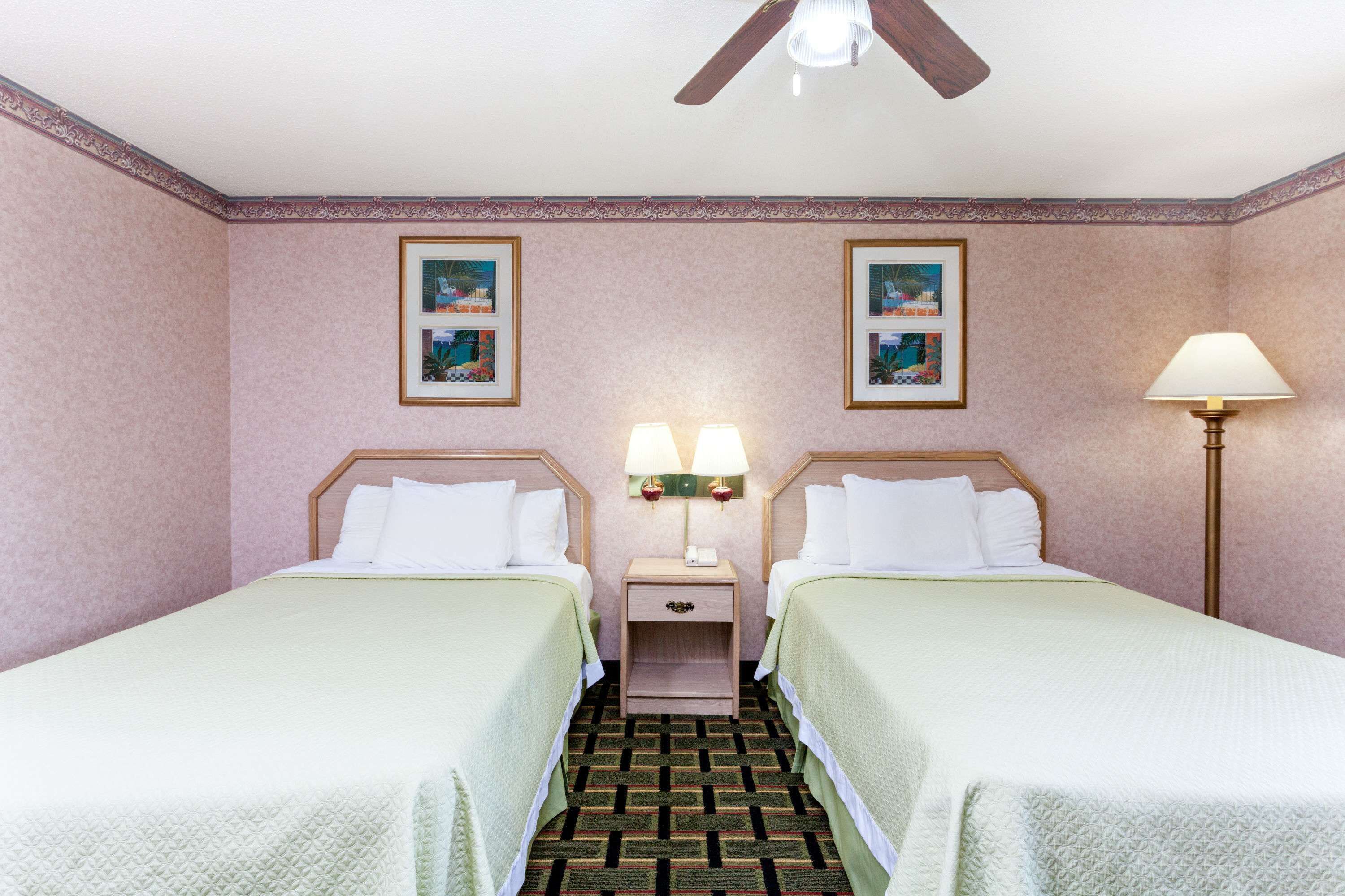 Una habitación de hotel con dos camas, una mesita de noche con lámparas y un ventilador de techo.