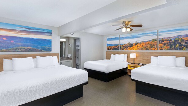 A hotel room with two beds, a ceiling fan, and large landscape paintings on the walls. - Days Inn by Wyndham Holladay (Holladay)