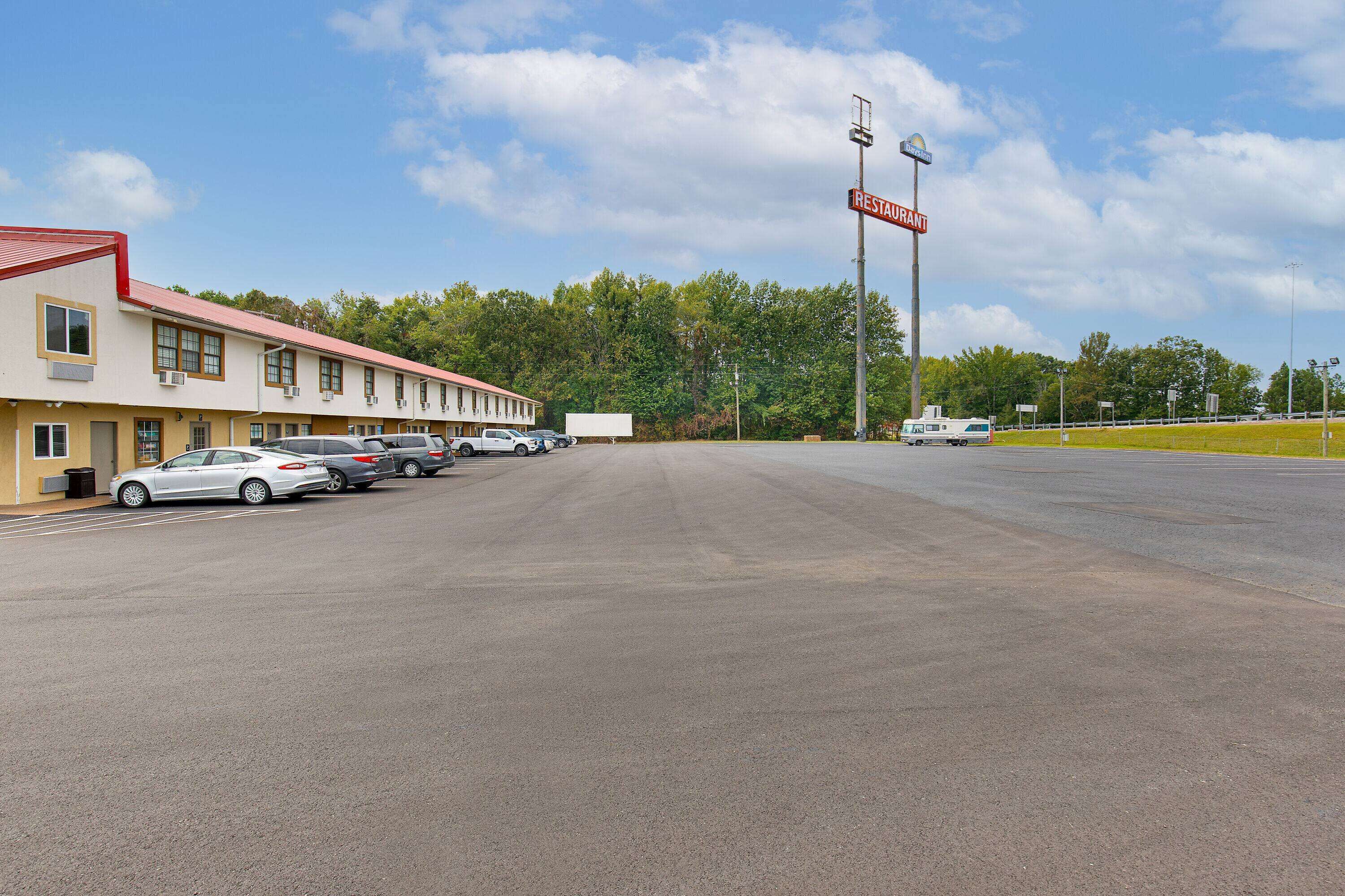 A motel with multiple rooms, a parking lot, and a restaurant sign in the background.