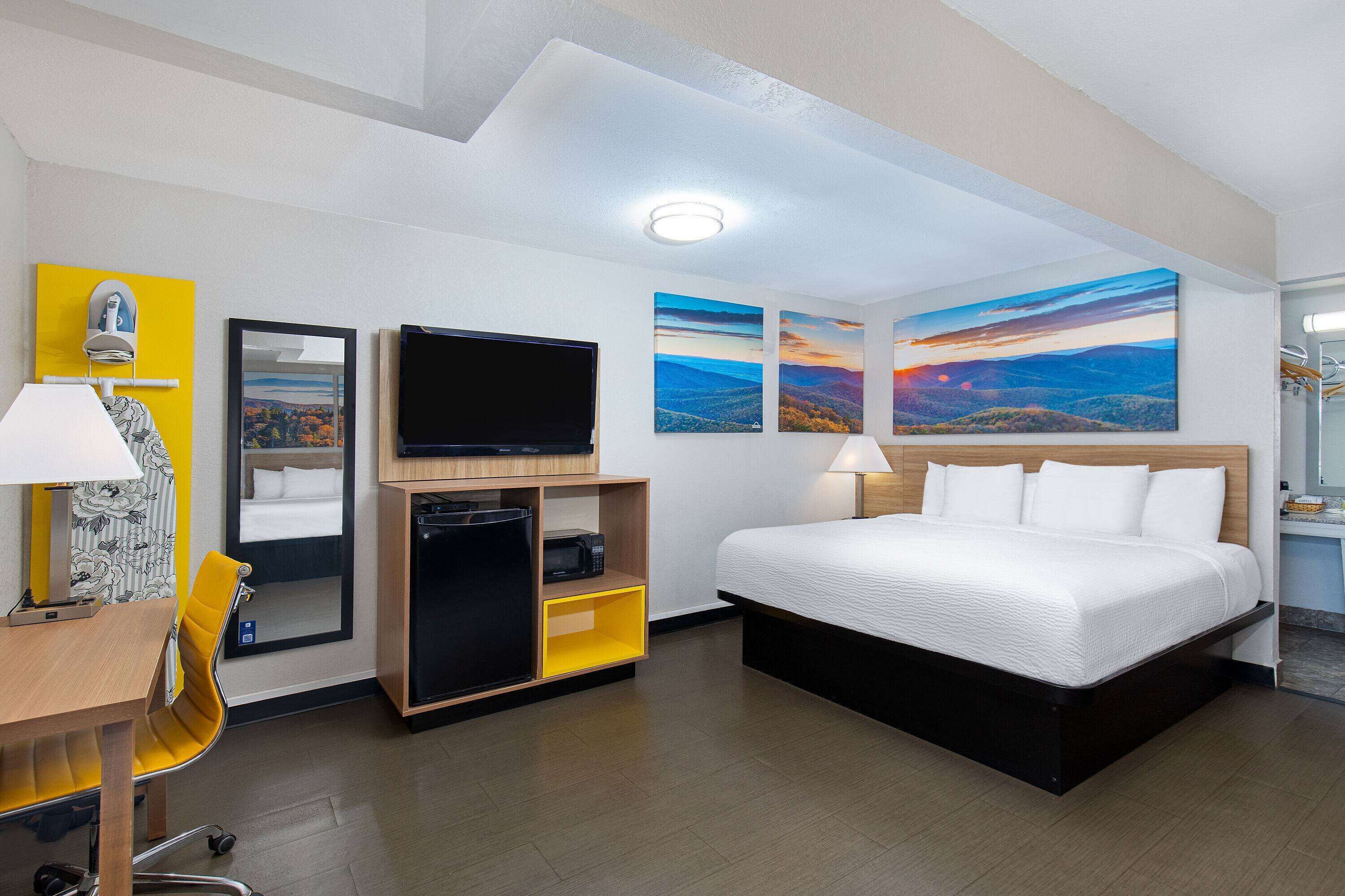 A hotel room with a bed, a desk with a chair, a television, and artwork on the walls.