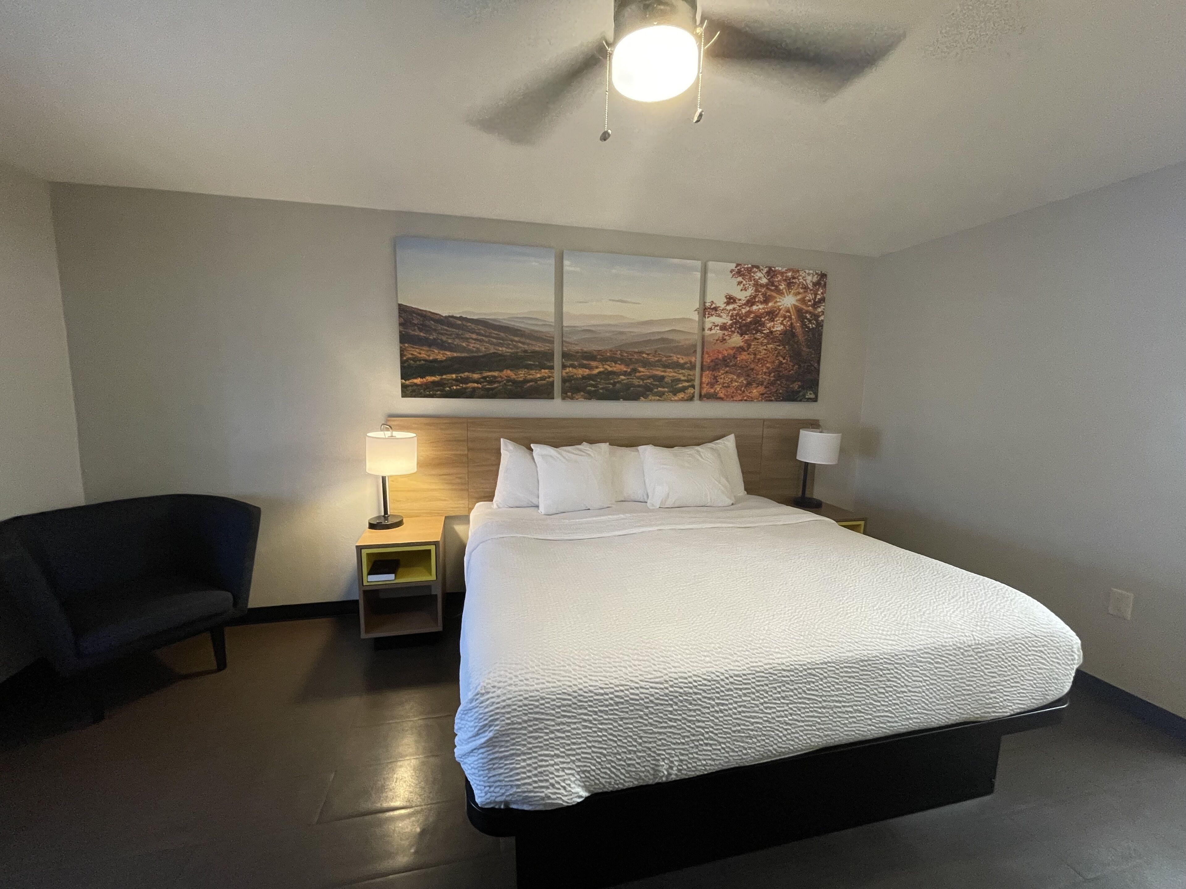 Ein Hotelzimmer mit einem großen Bett, zwei Nachttischen, einem Sessel und einem Deckenventilator.