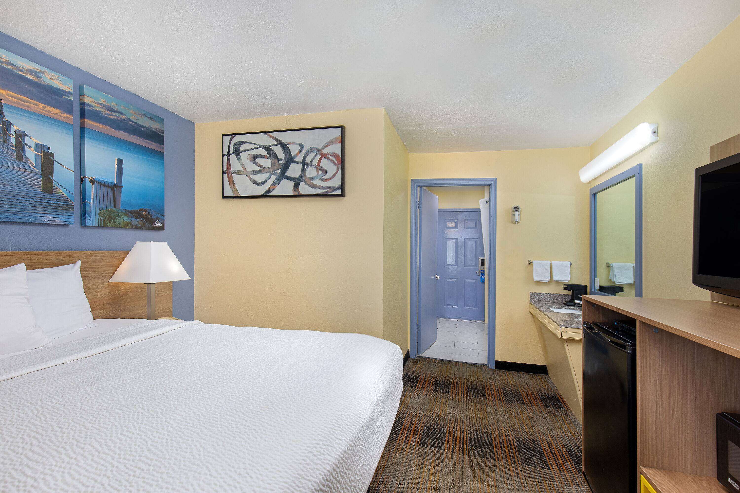 A hotel room with a bed, a desk with a television, a bathroom, and artwork on the walls.
