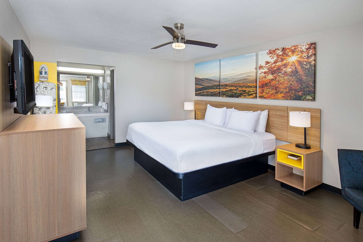 A hotel room with a bed, bedside tables, a TV, and a painting on the wall.