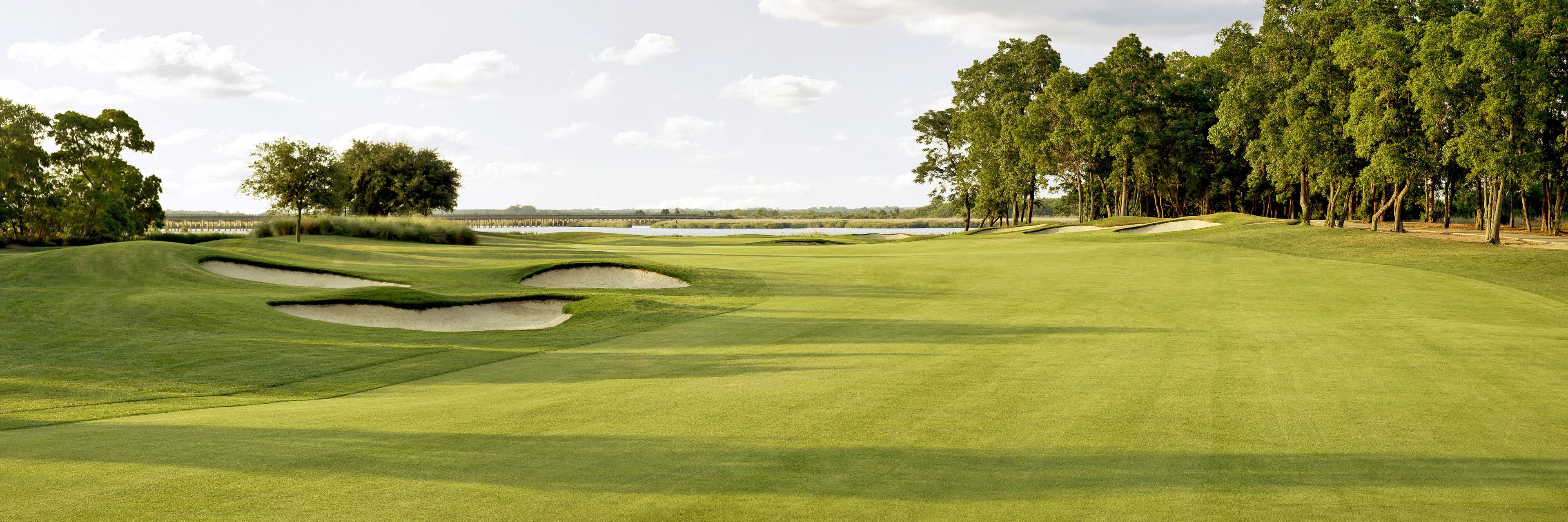 Un parcours de golf doté de bunkers de sable, d’un obstacle d’eau et d’une zone boisée.