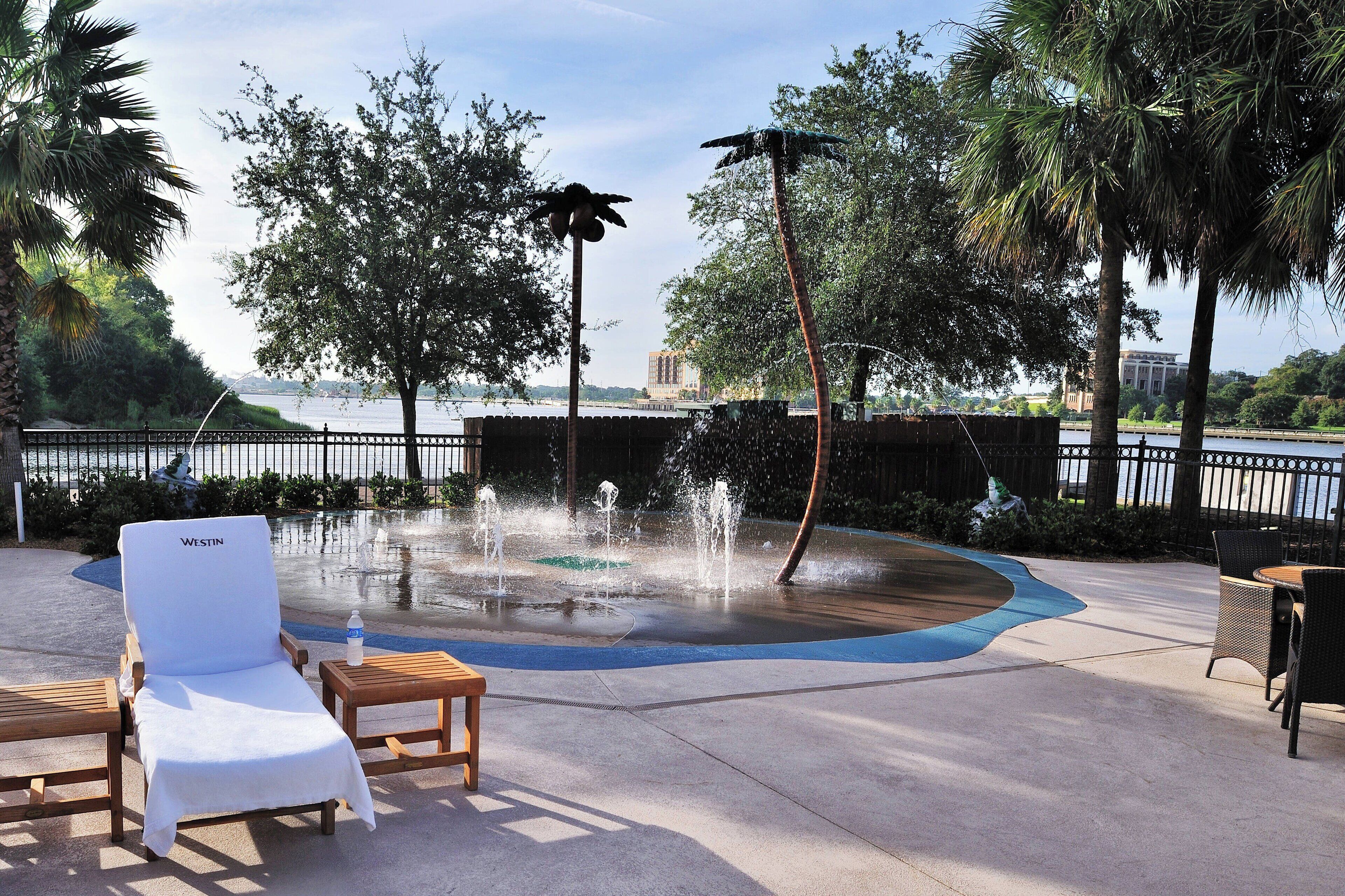 Uma área à beira da piscina com espreguiçadeira, mesa e um elemento decorativo de água.