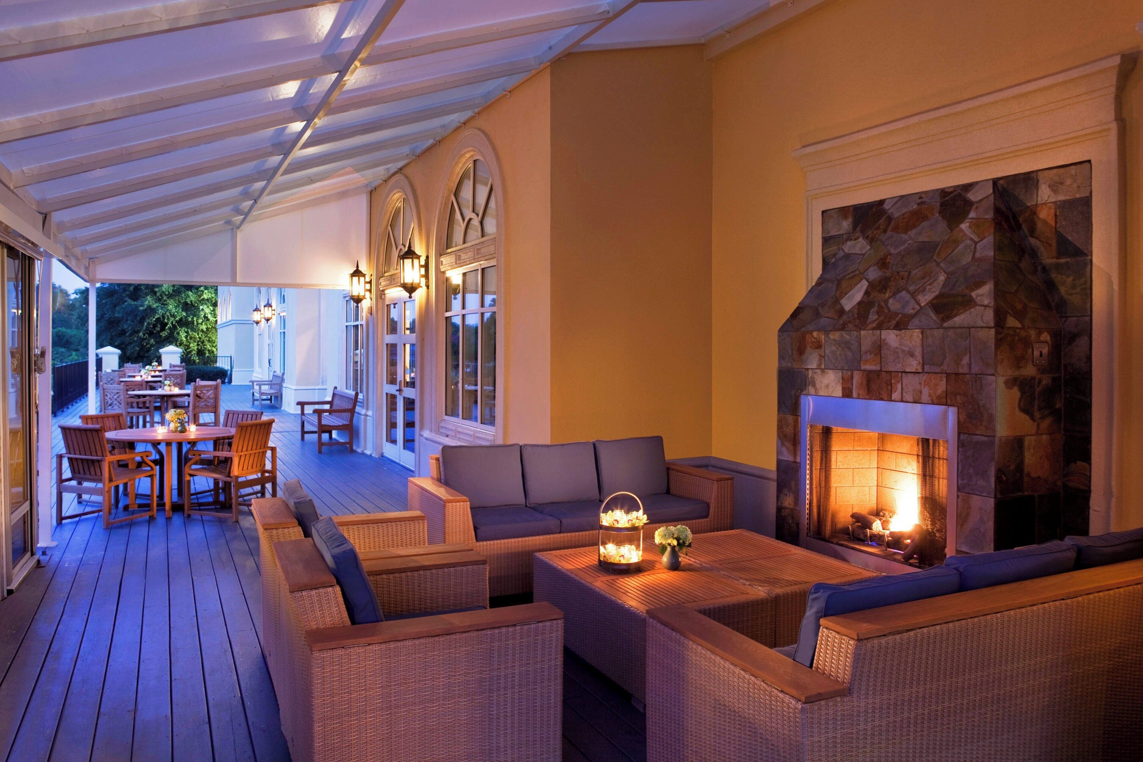 A covered outdoor seating area with wicker furniture, a stone fireplace, and a dining table with chairs.