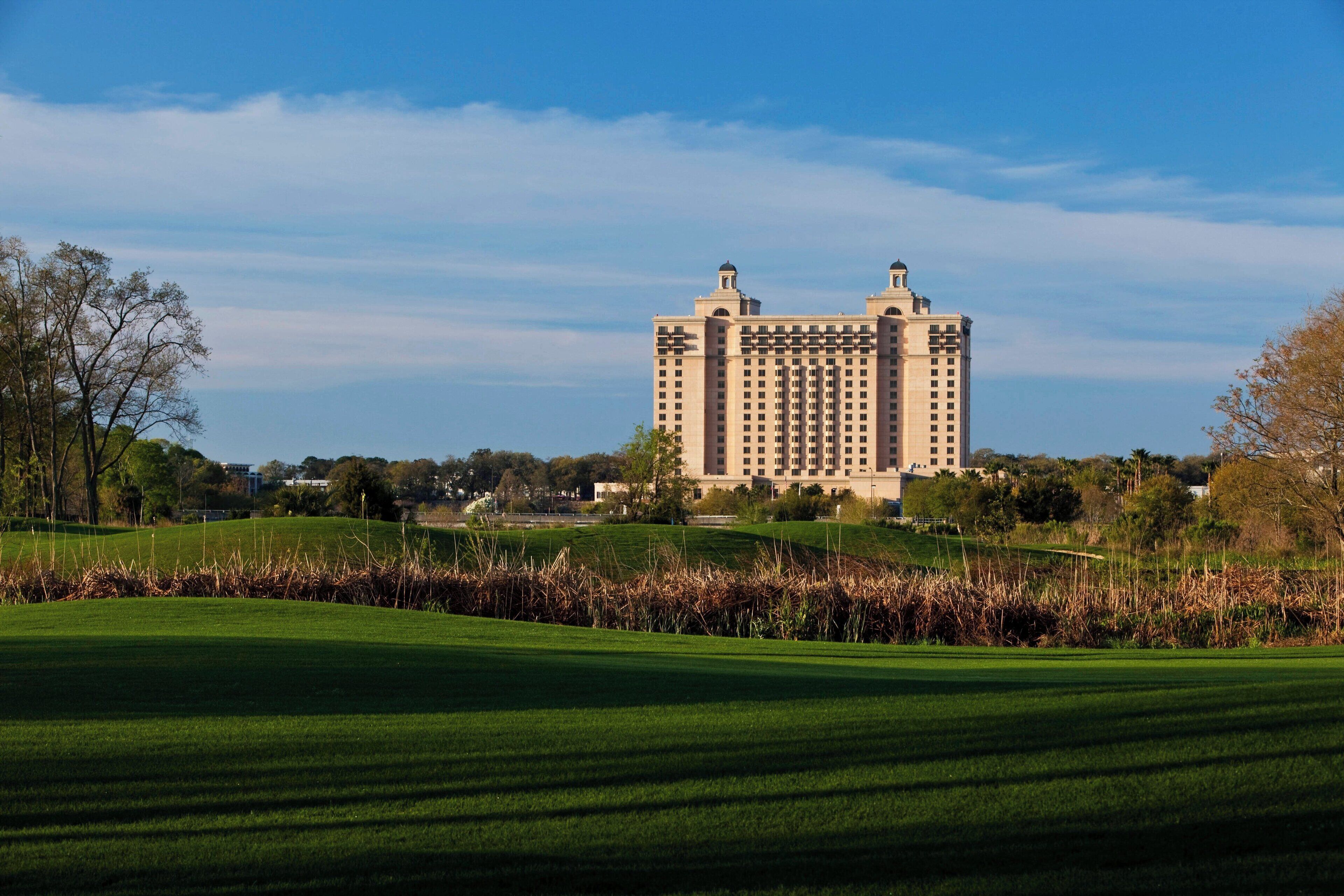 A large, multi-story hotel with a symmetrical facade, situated on a green landscape with a clear sky.